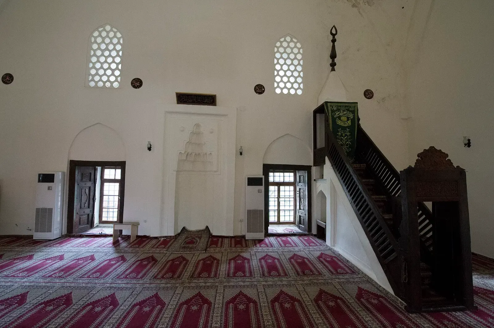 Het witte interieur van de Süleymaniye-moskee in Alanya met minbar en rode tapijten